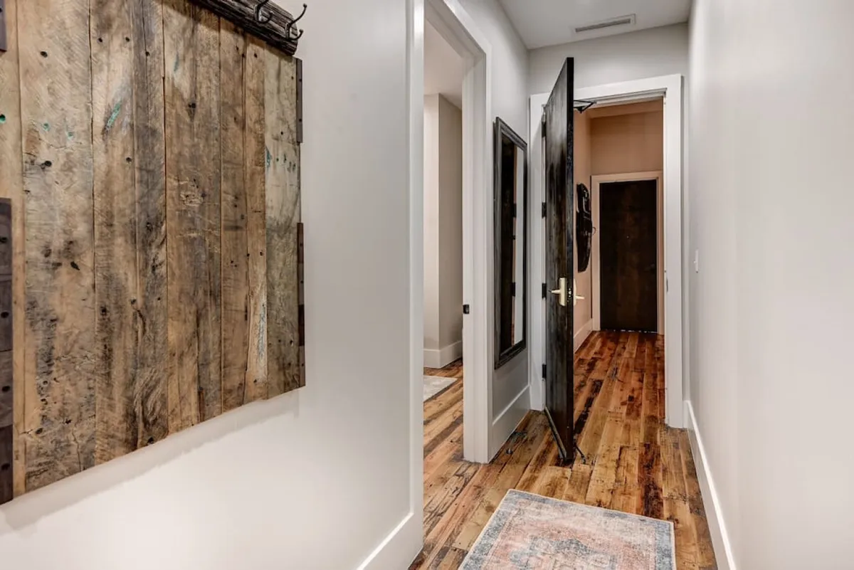 This image features a hallway with wooden wall art, an open door, and a mirrored wall. The scene suggests an inviting entry experience and easy navigation to other areas, evoking a smooth arrival and welcoming atmosphere.