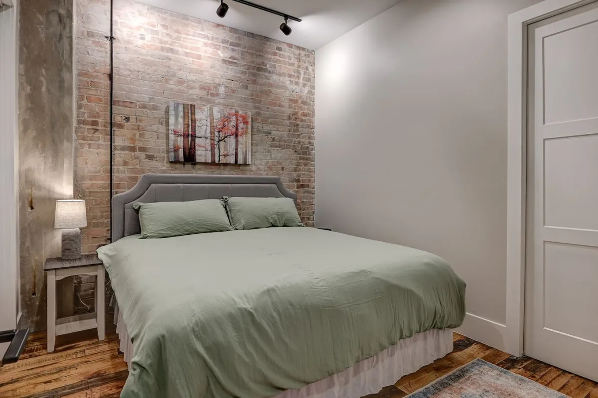 This image shows a tranquil bedroom with a plush bed dressed in green bedding, complemented by subtle wall art and a softly lit nightstand. The clean lines and gentle lighting evoke a sense of peace and relaxation.