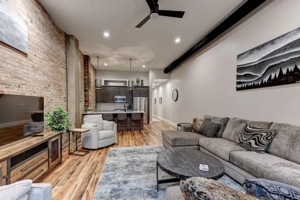 An open-plan living area highlighting a plush sofa, sleek coffee table, TV, and a modern kitchen in the background. Artwork on the wall and well-thought-out decor contribute to a contemporary feel, perfect for both entertaining guests and relaxing at home.