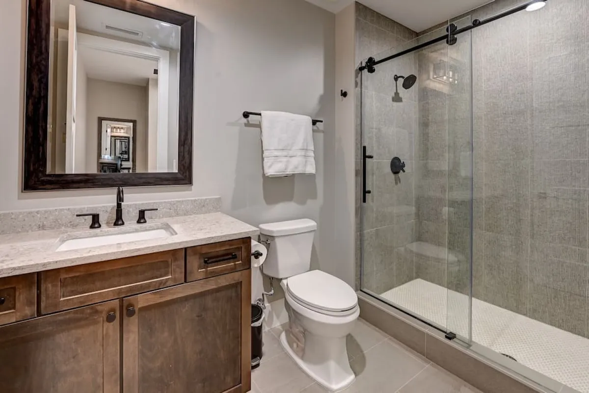 A sophisticated bathroom is displayed here, featuring a large mirror, elegant dark wood vanity, and a modern glass shower enclosure. The design balances historic charm with contemporary comfort, reflecting the en-suite amenities provided for both bedrooms.